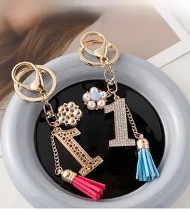 Détail macro du porte-clés numéro 1 doré avec strass et deux pompons colorés élégants