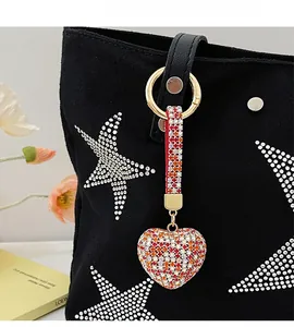 Close-up of heart-shaped keychain with colorful rhinestones hanging on a black canvas bag