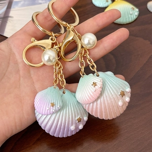 Porte-clés coquillage dégradé avec perle blanche et anneau doré sur bois sombre