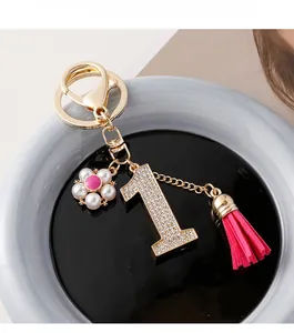 Gros plan sur le porte-clés numéro 1 serti de diamants avec pompon en cuir et fleur rose