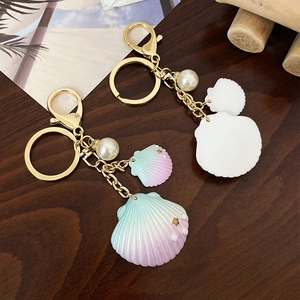 Porte-clés coquillage dégradé avec perle blanche et fermoir doré sur fond de bois