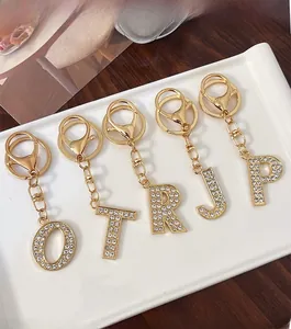 Detail of five gold alloy alphabet keychains with white rhinestones on white tray