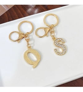 Detail of golden Q and S alphabet keychains with brushed texture and sparkling rhinestones