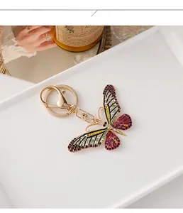 Détail d'un porte-clés papillon doré orné de strass colorés sur un plateau décoratif blanc
