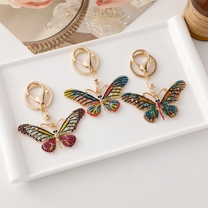 Porte-clés papillon chic avec strass colorés sur un plateau en céramique blanche