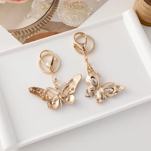 Porte-clés papillon doré avec strass brillants et breloques en métal sur plateau blanc