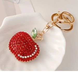 Close-up of a sparkling red rhinestone apple keychain with gold metal hardware on a tray