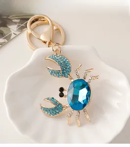 Détail du porte-clés crabe 3D avec cristal bleu et strass dans un bol en coquillage