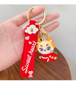 Close-up of a cartoon dragon keychain with a red Sweet Heart strap and gold metal clasp