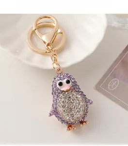 Détail d'un porte-clés pingouin mignon avec cristaux violets sur une base en métal doré