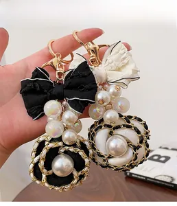 Detailed close-up of camellia bow keychain with elegant faux pearls and woven metal chain
