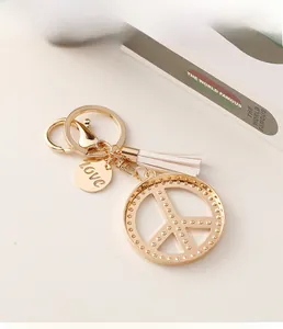 Detail of peace sign keychain with white tassel and LOVE engraved gold pendant