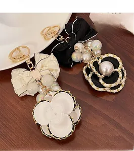 Detail shot of a black fabric bow and camellia charm keychain on a gold-tone metal ring