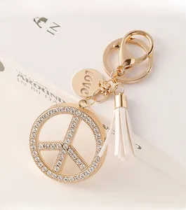 Close-up of golden peace sign keychain with inlaid rhinestones and white leather tassel