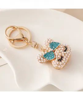 Close-up of pearl-studded rabbit head keychain with a blue rhinestone bow in a shell tray