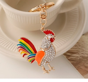 Enamel rooster keychain with colorful feathers and white crystals on a ceramic cup