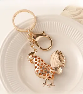 Detailed close-up of a golden metal rooster keychain with hollow heart pattern