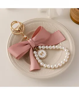 Close-up of pink fabric bow keychain with cream pearls and golden embossed charm detail