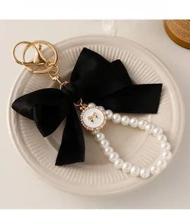 Macro shot of large black satin bow keychain with white faux pearls and gold hardware