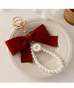 Detail of burgundy velvet bow keychain with white pearls on a ceramic tray