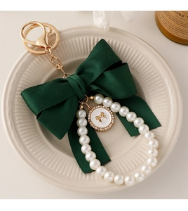 Detailed shot of dark green bow keychain with white pearls and golden charm on a tray
