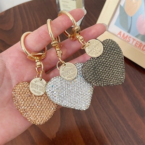 Sparkling rhinestone heart keychains in champagne, silver, and grey on a wood desk