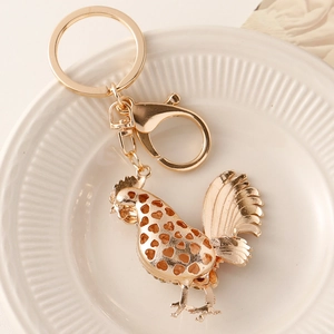 Golden alloy rooster keychain with hollow heart pattern on elegant white plate