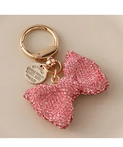 Close-up of pink crystal bow keychain with gold spring ring and engraved metal tag