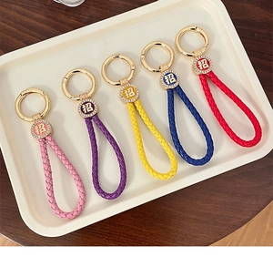 Detail of five colorful woven leather rope keychains with gold charms and lucky symbols
