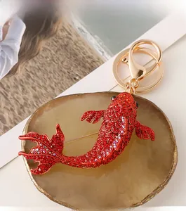 Détail macro de la broche carpe en strass rouge et porte-clés doré avec fermoir
