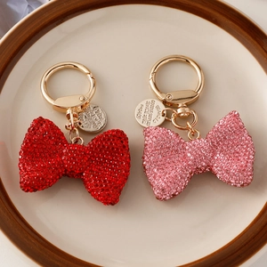 Red and pink crystal bow keychains with gold metal hardware in a ceramic tray