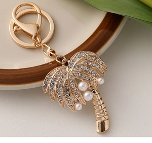 Macro view of gold coconut tree keychain with rhinestones and white pearls on a tray