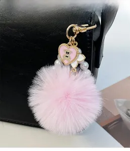 Porte-clés pompon rose avec pendentif cœur ours doré et perles sur un sac noir élégant