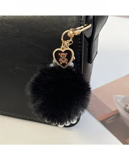 Détail du porte-clés pompon noir avec pendentif cœur d'ours doré sur un sac en cuir