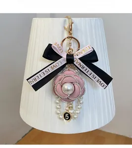 Détail du porte-clés camélia rose avec chaînes de perles, strass et élégant nœud en ruban