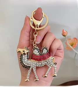 Detailed close-up of a golden camel keychain with white rhinestones and red enamel saddle