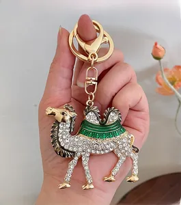 Detail of hand-held golden camel keychain with white rhinestones and green enamel flower