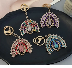 Peacock keychains in four color variants displayed on a luxury black decorative plate
