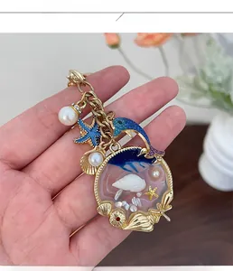 Detailed close-up of golden ocean keychain with blue dolphin and resin shell pendant