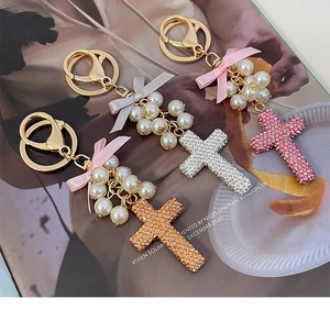 Detail view of pearl cross keychain with sparkling rhinestones and silk bow accents