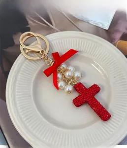 Close-up of red rhinestone cross keychain with white pearls and a silk bow on a ceramic plate