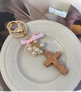 Detail of cross charm with champagne rhinestones, white pearls and pink bow on a gold keychain
