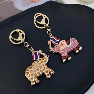 Golden elephant keychain with rhinestones and Thailand flag charms on a black tray