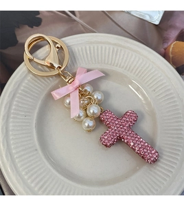 Detail of pink rhinestone cross charm with pearls and silk bow on gold keychain