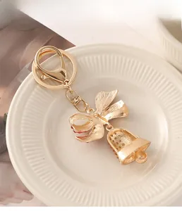 Detailed close-up of a gold bow bell keychain decorated with small rhinestones on a tray