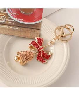 Close-up of Christmas bell keychain with red bow and champagne rhinestones on ceramic tray