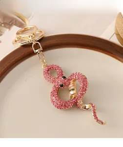 Detailansicht eines goldenen Schlangen-Schlüsselanhängers mit rosa Kristallen auf Porzellan