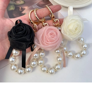 Detailed macro of handmade lace rose and pearl keychains in white, pink, and black colors