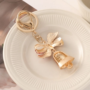 Golden Christmas bell keychain with bowknot and red rhinestones on a decorative white plate