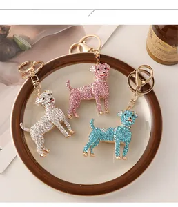 Three crystal-studded dog keychains in white, pink, and blue colors on a tray